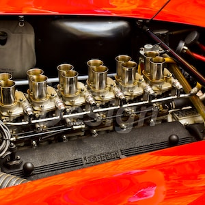 May include: Close-up of a classic car engine with multiple chrome-plated carburetors and the word "Ferrari" visible on the engine block.