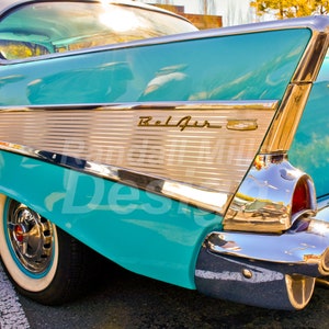 May include: A turquoise blue 1957 Chevrolet Bel Air with chrome trim and a whitewall tire. The car has a chrome rear bumper and tail lights. The car has a chrome trim piece with the word "Bel Air" on it.