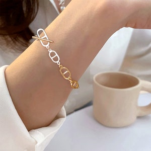 May include: A gold and white bracelet with a chain link design. The bracelet features a toggle clasp.