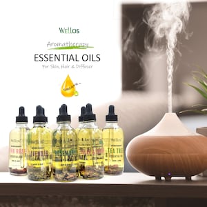 May include: Six small glass bottles of essential oils with dropper tops. The bottles are labeled with the names of the oils: Pink Rose, Lavender, Rosemary, Orange & Ginger, and Tea Tree. The bottles are arranged in a row on a wooden surface. A wooden essential oil diffuser is in the background.