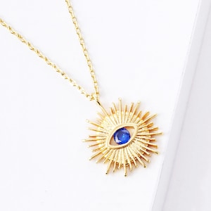 May include: A gold necklace with a blue evil eye pendant surrounded by a sunburst design.