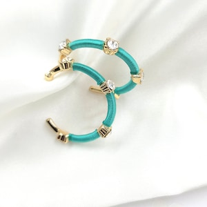 May include: A pair of turquoise hoop earrings with gold accents and clear rhinestones.