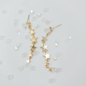 May include: A pair of gold star-shaped dangle earrings. Each earring features a chain of connected stars.