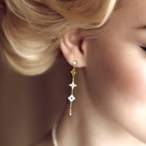 May include: Gold dangle earrings with a small clear stone at the top and a series of white and gold flower-shaped charms hanging down.