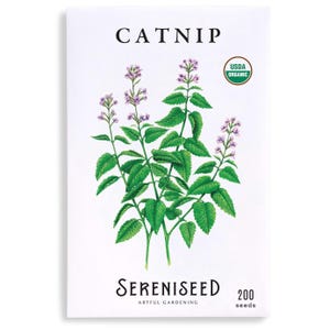 May include: A packet of catnip seeds with a botanical illustration of the plant. The packet is white with the word "CATNIP" at the top and "Sereniseed Artful Gardening" at the bottom. A "USDA Organic" seal is visible.