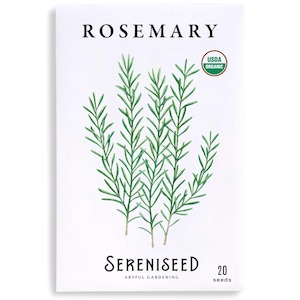 May include: A white seed packet with the word "ROSEMARY" at the top and a watercolor illustration of rosemary sprigs. The packet also includes the text "Sereniseed Artful Gardening" and "20 seeds". A USDA Organic seal is in the upper right corner.
