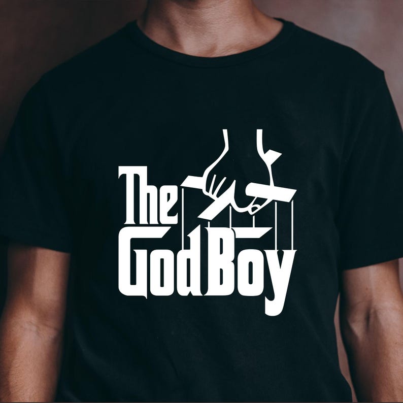 May include: Black t-shirt with a white graphic that reads "The GodBoy" in a stylized font, with a hand holding puppet strings. The design is a parody of the movie "The Godfather".