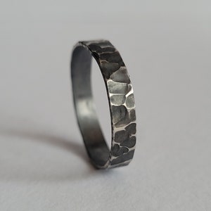 Könnte beinhalten: Ein silberner Ring mit gehämmerter Textur. Der Ring ist breit und hat ein abgerundetes Profil.