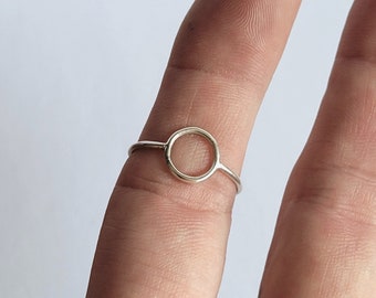 May include: A simple silver ring with a circular design. The ring is worn on a finger.
