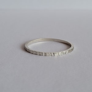 Könnte beinhalten: Ein dünner Silberring mit einem strukturierten Rand.