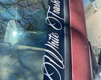Könnte beinhalten: Ein weißer Vinyl-Aufkleber mit dem Text "All White Trash" in einer kursivschriftlichen Schriftart, der auf die Heckscheibe eines Autos geklebt ist.