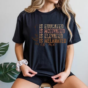 Puede incluir: Camiseta negra con el texto "She is Educated, Is Motivated, Is Elevated, Is Melanated, is me" en letras marrones y beige. La camiseta es de cuello redondo.