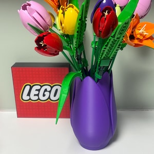May include: A colourful bouquet of LEGO tulips in a purple vase. The flowers are in shades of pink, orange, yellow, and red, with green stems and leaves. A red box with the LEGO logo is visible.