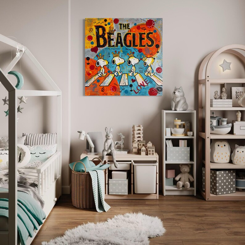 May include: A colorful pop art style canvas print titled "The Beagles" featuring Snoopy and his friends crossing a street. The artwork has a vibrant mix of orange, yellow, blue, and red. The nursery decor includes a white crib and a wooden bookshelf.