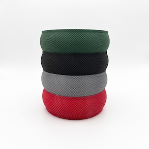 May include: A stack of four wide headbands featuring a textured, grid-like pattern. The headbands are arranged vertically in colors of dark green, black, gray, and red, each displaying a consistent woven-style surface finish.