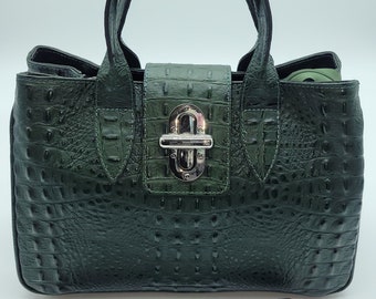 May include: A dark green leather handbag with a crocodile embossed pattern. The bag has a top handle and a detachable shoulder strap. The bag has a silver lock and hardware.