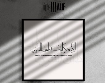 May include: Black framed wall art with Arabic calligraphy. The artwork features elegant black script on a white background, with the English translation "Verily in the remembrance of Allah do hearts find peace." The artist's logo is in the top left corner.