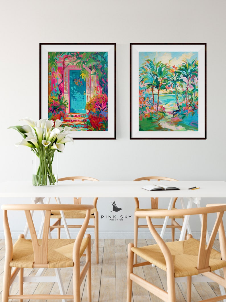 May include: Two framed paintings on a white wall. The painting on the left shows a blue door with a pink and green floral design. The painting on the right shows a beach scene with palm trees and a turquoise ocean.