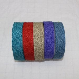 Peut inclure: Un rouleau de six bandeaux en tissu colorés. Les bandeaux sont dans les tons de turquoise, rouge, beige, violet et bleu denim. Chaque bandeau a un aspect texturé.
