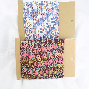 Peut inclure: Deux rouleaux de ruban en tissu à motifs floraux sur des bobines en carton brun. Le rouleau du haut est blanc avec des fleurs bleues et roses. Le rouleau du bas est marron avec des fleurs roses, vertes et dorées.