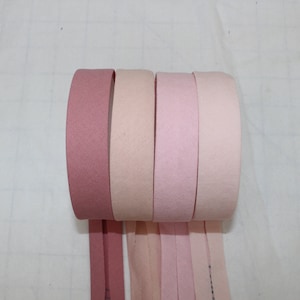 Può includere: Quattro rotoli di nastro rosa in diverse tonalità di rosa, dal scuro al chiaro. Il nastro è arrotolato e le estremità pendono.