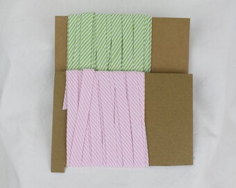May include: Two spools of striped fabric ribbon. One spool is green and white, the other is pink and white.