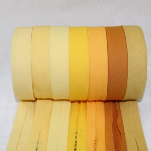 May include: A roll of fabric ribbon in various shades of yellow, from pale cream to deep golden brown. The ribbon is unfurled, showing the different colors.