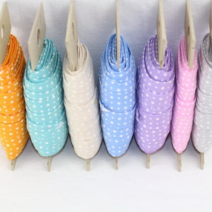 May include: A selection of polka dot ribbons in various colours, including orange, turquoise, cream, pale blue, lilac, pink, and grey. Each ribbon is rolled and attached to a cardboard display. Ideal for crafts and gift wrapping.
