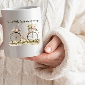 May include: White ceramic mug with a floral design and a bicycle with the text "two wheels, fresh air, no cares".