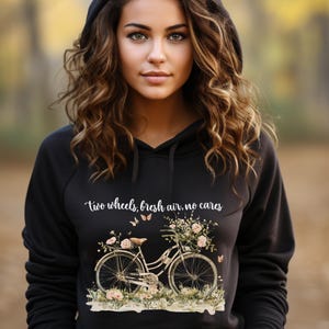 May include: Black hoodie with a white graphic of a bicycle with flowers and butterflies. The text "two wheels, fresh air, no cares" is printed on the hoodie.