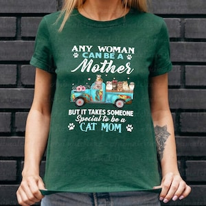 Puede incluir: Camiseta verde oscuro con el texto "ANY WOMAN CAN BE A Mother BUT IT TAKES SOMEONE Special to be a CAT MOM." El dise&ntilde;o incluye un cami&oacute;n azul con gatos y flores.