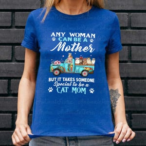 Puede incluir: Camiseta azul con el texto "ANY WOMAN CAN BE A Mother BUT IT TAKES SOMEONE Special to be a CAT MOM". El dise&ntilde;o muestra una camioneta turquesa con gatos y flores.