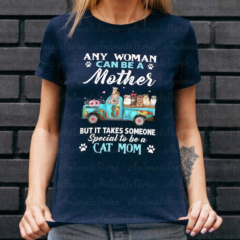 Puede incluir: Camiseta azul marino con el texto "ANY WOMAN CAN BE A Mother" y "BUT IT TAKES SOMEONE Special to be a CAT MOM". El dise&ntilde;o presenta un cami&oacute;n azul con gatos y flores.