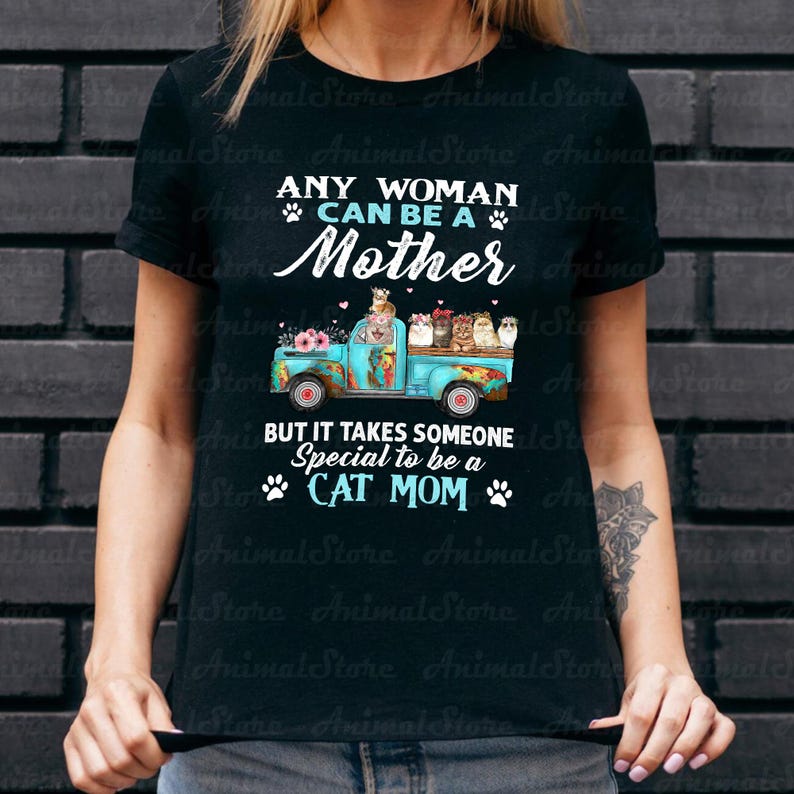 Puede incluir: Camiseta negra con el texto "ANY WOMAN CAN BE A Mother, BUT IT TAKES SOMEONE Special to be a CAT MOM." Una camioneta turquesa est&aacute; llena de gatos y flores.
