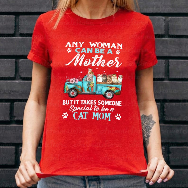 Puede incluir: Camiseta roja con el texto "ANY WOMAN CAN BE A Mother BUT IT TAKES SOMEONE Special to be a CAT MOM." Un gr&aacute;fico de cami&oacute;n azul transporta gatos y flores. La camiseta est&aacute; hecha de un material suave.