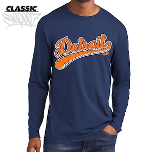 May include: A navy blue long-sleeve t-shirt with an orange graphic of the word "Detroit" in a baseball-style font with a baseball bat behind the text.