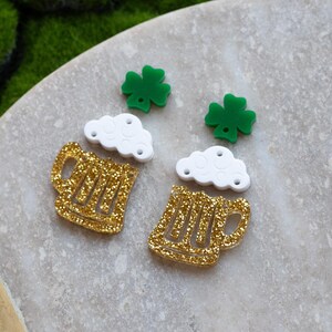 May include: A pair of gold glitter beer mug earrings with white foam and green shamrock charms.