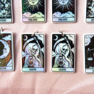 Puede incluir: Un juego de diez cartas de tarot iridiscentes con ilustraciones en blanco y negro. Las cartas presentan los siguientes t&iacute;tulos: Los Enamorados, El Sol, La Fuerza, La Luna, La Muerte, La Justicia.