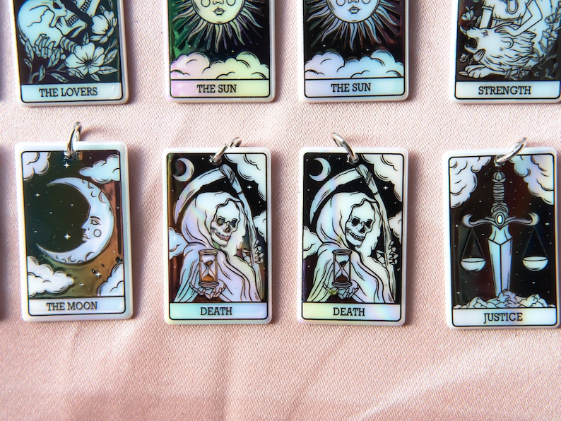 Puede incluir: Un juego de diez cartas de tarot iridiscentes con ilustraciones en blanco y negro. Las cartas presentan los siguientes t&iacute;tulos: Los Enamorados, El Sol, La Fuerza, La Luna, La Muerte, La Justicia.