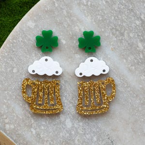 May include: A pair of gold glitter beer mug earrings with white foam and green shamrock charms.