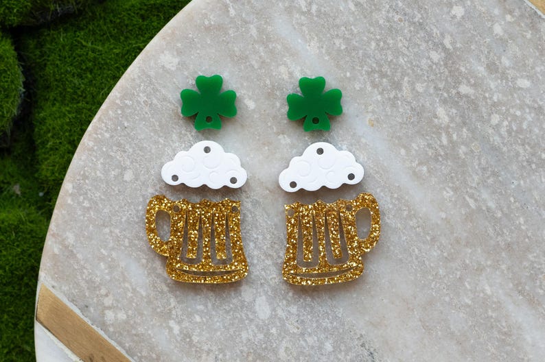 May include: A pair of gold glitter beer mug earrings with white foam and green shamrock charms.