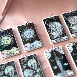 Puede incluir: Un conjunto de ocho amuletos de cartas del tarot iridiscentes que presentan varias im&aacute;genes de cartas del tarot, incluyendo El Sol, la Fuerza y ​​la Justicia. Los amuletos est&aacute;n hechos de acr&iacute;lico blanco y tienen un acabado hologr&aacute;fico.