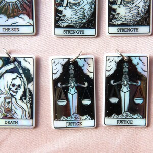 Puede incluir: Conjunto de diez cartas de tarot con acabados iridiscentes. Las cartas presentan im&aacute;genes del Sol, la Fuerza, la Muerte, la Justicia y una segunda carta de Justicia. Las cartas son blancas con detalles negros y plateados.
