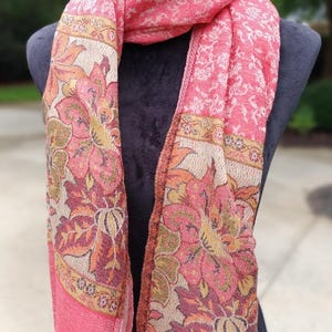 May include: A pink and cream floral patterned scarf with a paisley design. The scarf is made of a soft, lightweight fabric and is perfect for adding a touch of elegance to any outfit.