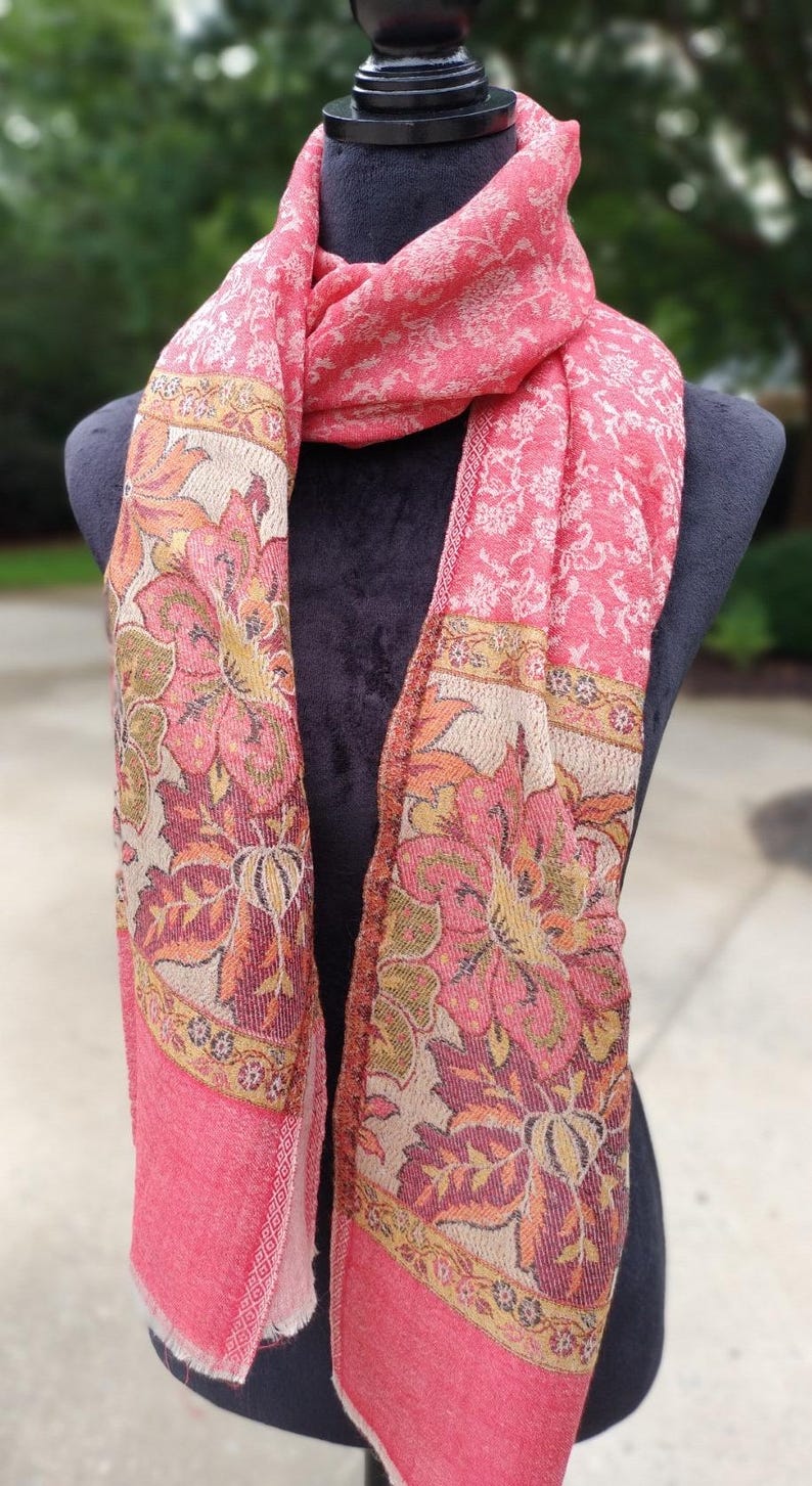 May include: A pink and cream floral patterned scarf with a paisley design. The scarf is made of a soft, lightweight fabric and is perfect for adding a touch of elegance to any outfit.