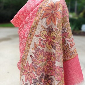 May include: A pink and cream floral patterned shawl with a fringed edge. The shawl is draped over a mannequin.