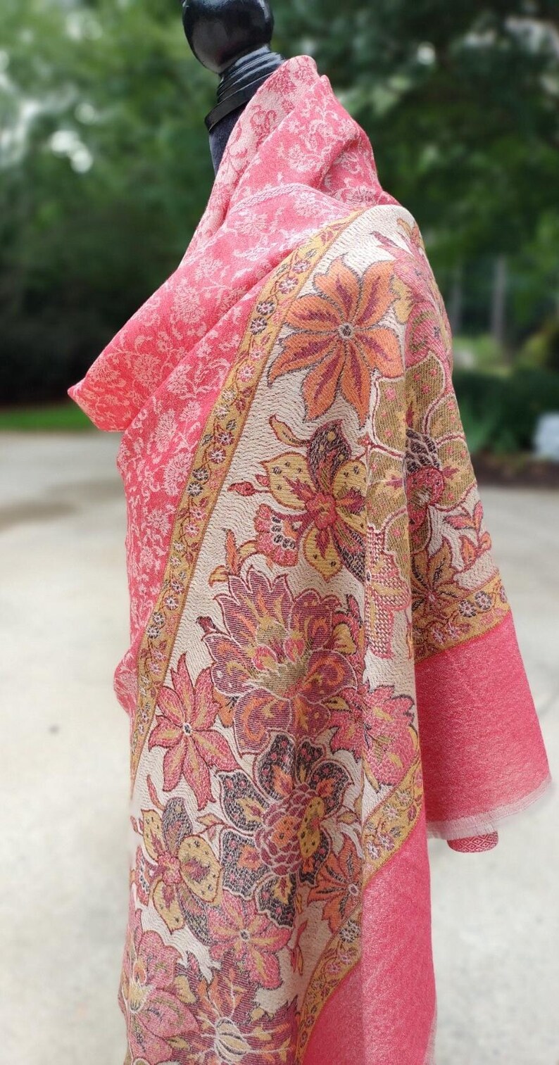 May include: A pink and cream floral patterned shawl with a fringed edge. The shawl is draped over a mannequin.