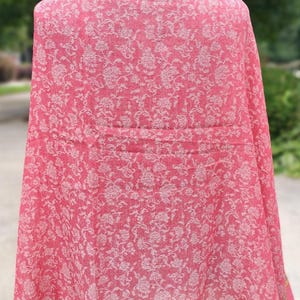 May include: A pink shawl with a white floral pattern. The shawl is draped over a mannequin and has a fringed edge.