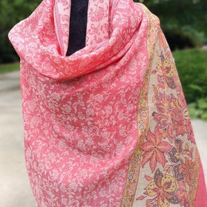 May include: A pink shawl with a white floral pattern and a beige border with a floral design. The shawl is draped over a mannequin.