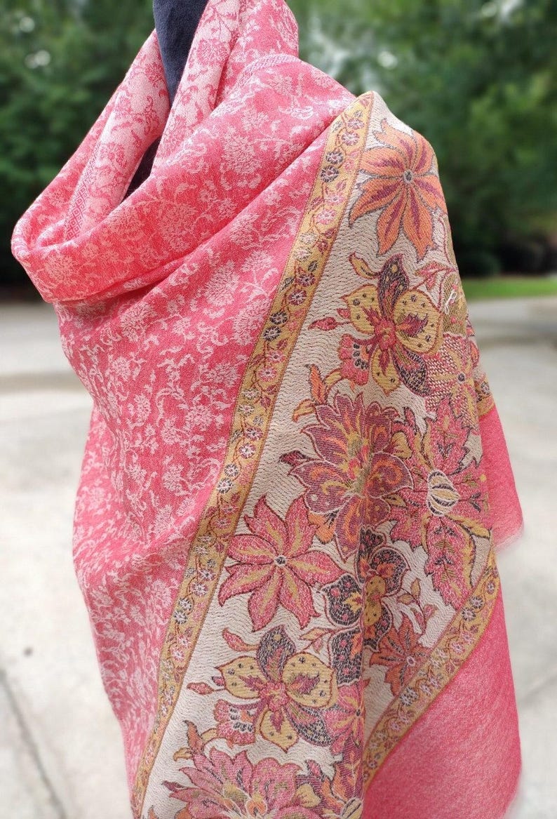 May include: A pink and cream floral patterned shawl with a gold border. The shawl is made of a soft, lightweight fabric and is perfect for adding a touch of elegance to any outfit.